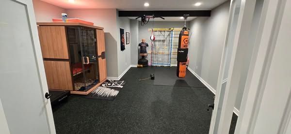 Home gym with sauna, punching bag, and exercise equipment. Gray walls, black flooring.