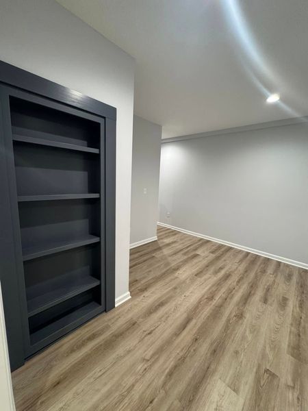 Built-in bookshelf with dark frame, next to an empty room with wood-look flooring and light gray walls.