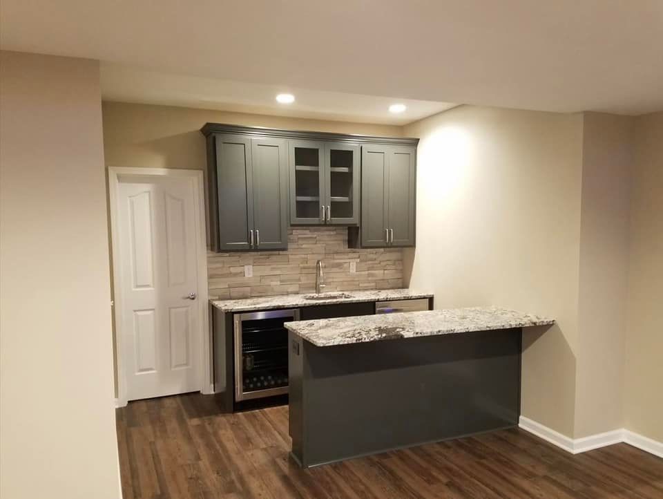 Basement bar with gray cabinets, granite countertop, sink, and mini-fridge.