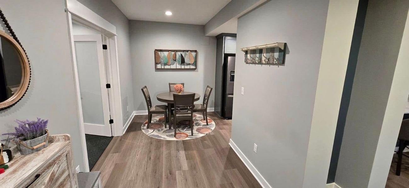 A dining area with a round table, chairs, art, and a rug. Light gray walls with a matching floor.