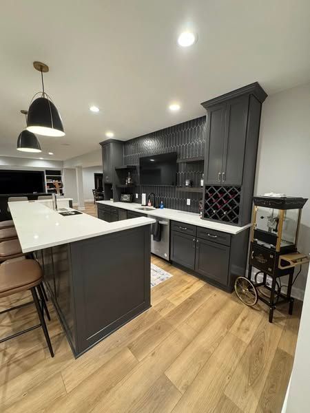 Modern gray kitchen with white countertops and wooden floor. Includes a bar, wine rack, and popcorn machine.