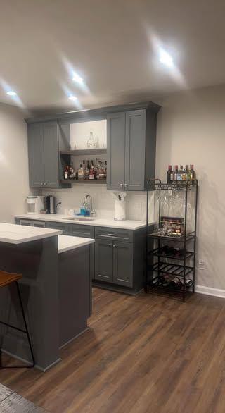 Gray cabinets and island in a modern kitchen with a wine rack and wood-look flooring.