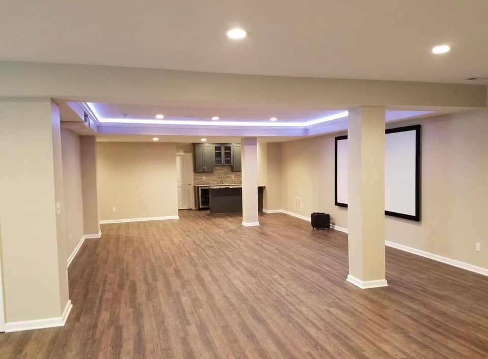Finished basement with hardwood-style flooring, recessed lighting, and a small bar area; a projector screen hangs on the wall.