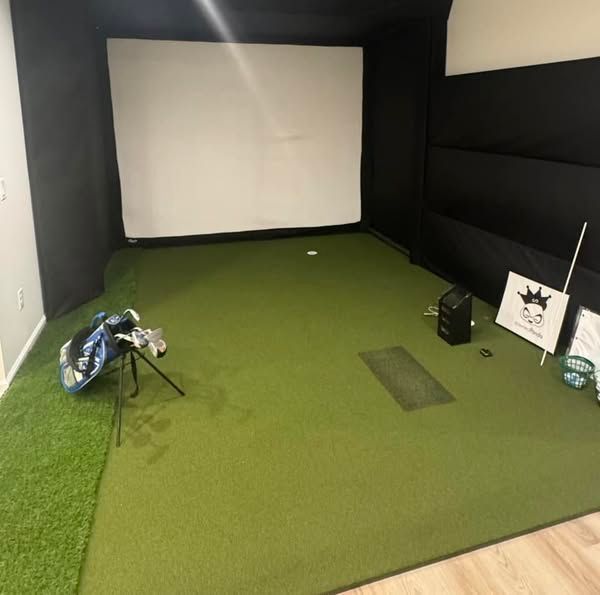Golf simulator setup with a screen, turf, and golf bag.