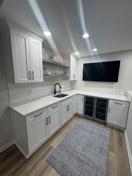 White bar area with cabinets, sink, countertop, wine cooler, TV, and gray rug.