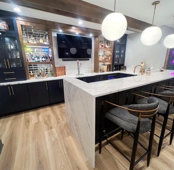Stylish home bar with black cabinets, marble countertops, and round pendant lights.