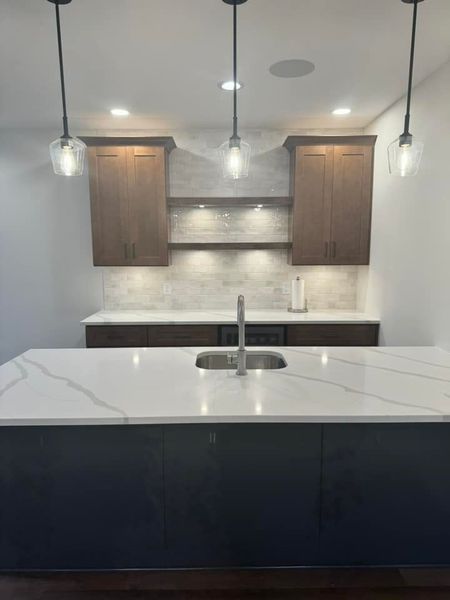 Modern kitchen with dark cabinetry, white countertop, and pendant lights.