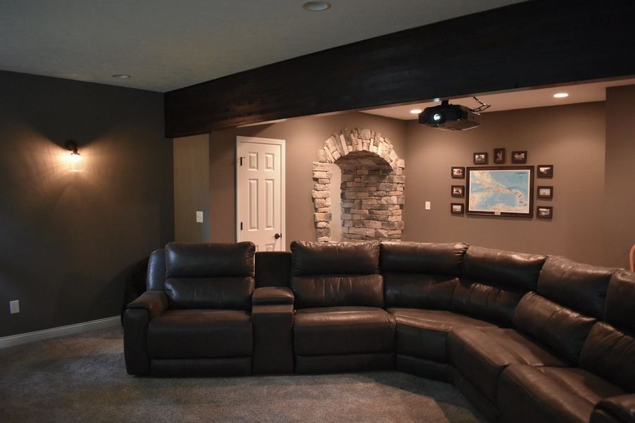A dark brown sectional sofa in a home theater, with a stone accent and a projector.