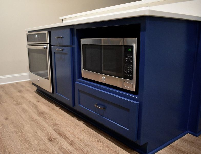Blue kitchen island with built-in microwave, oven, and cabinetry on wood-look flooring. White countertop.