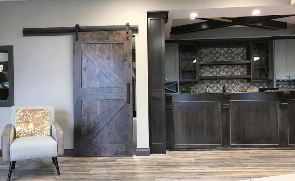 Barn door in a room with a bar, gray and white decor, and an armchair.
