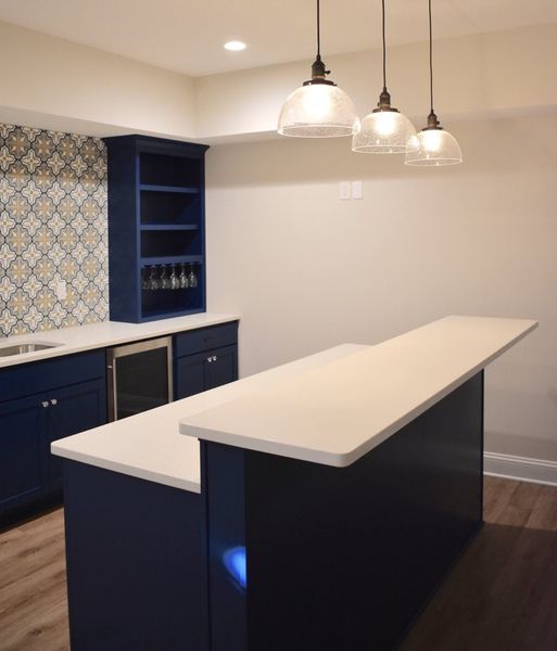 Blue and white home bar with quartz countertops, pendant lights, and a tiled backsplash.