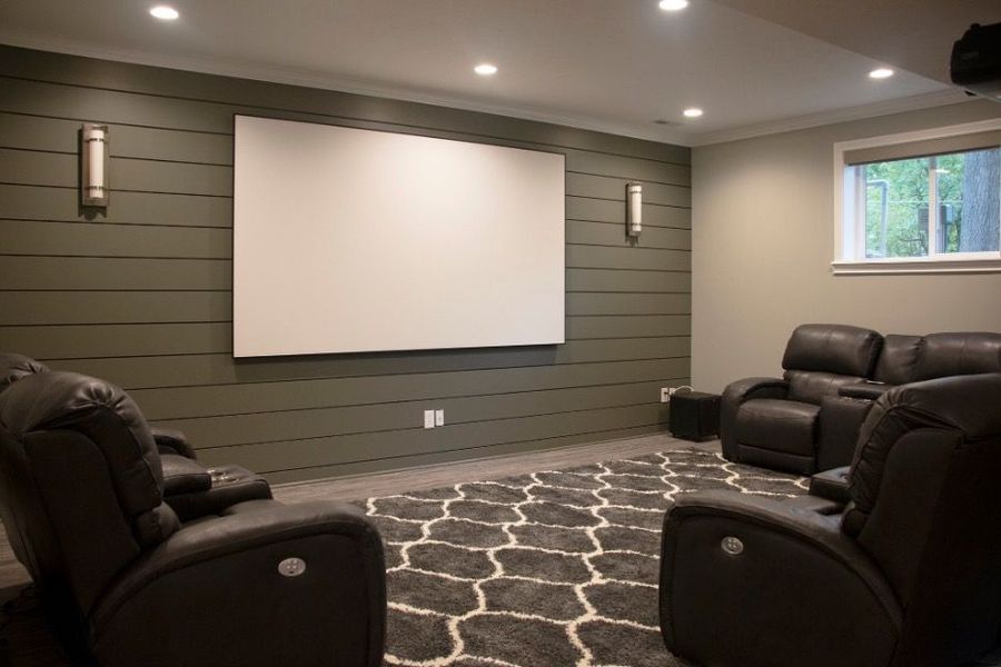 Home theater room with screen on green wall, black recliners, and patterned rug.