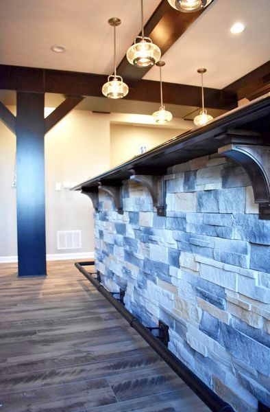 Bar with stone facade, dark wood trim, pendant lights, and wood flooring.