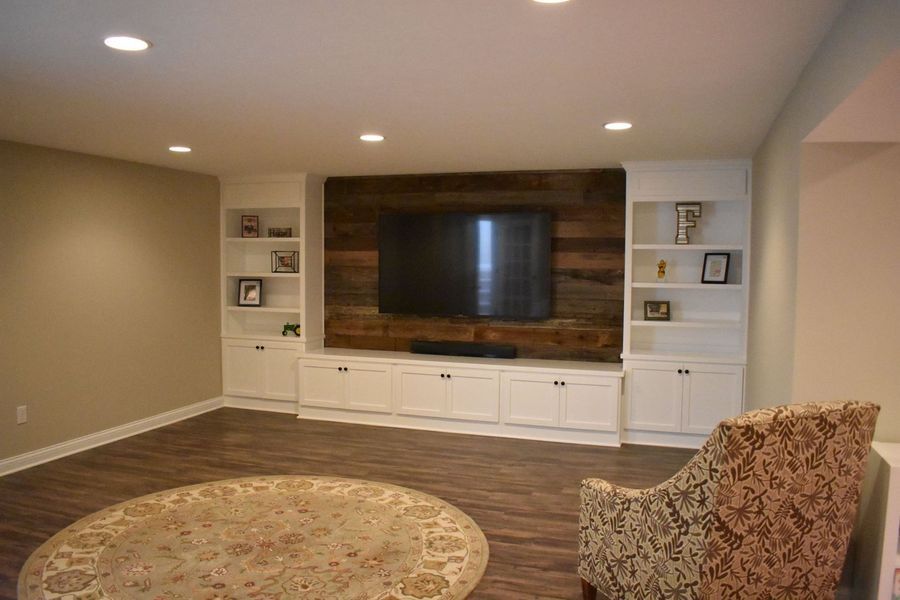 Living room with built-in white cabinets, TV on wood wall, area rug, and patterned armchair.