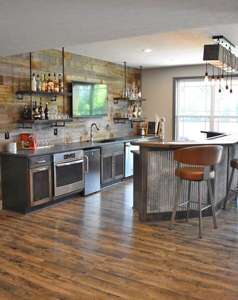 Rustic home bar with wood paneling, shelves with liquor bottles, sink, appliances, and bar stools.