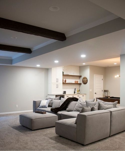 Modern basement living room with gray sectional sofa, ottoman, and bar area.