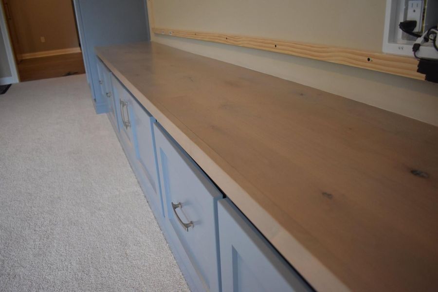 Long wooden countertop on blue cabinets against a beige wall, a room with carpet.
