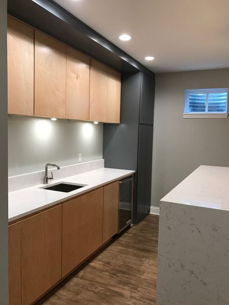 Modern kitchenette with light wood cabinets, white countertops, and stainless steel sink.