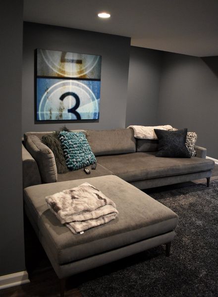 Gray sectional sofa in a dark gray room, with pillows and a folded blanket. Film reel art on the wall.