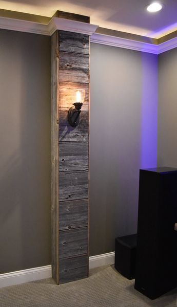 Column clad in weathered wood with a sconce against a gray wall.