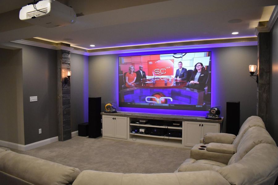 Home theater with large screen, speakers, and plush seating, displaying a news program.