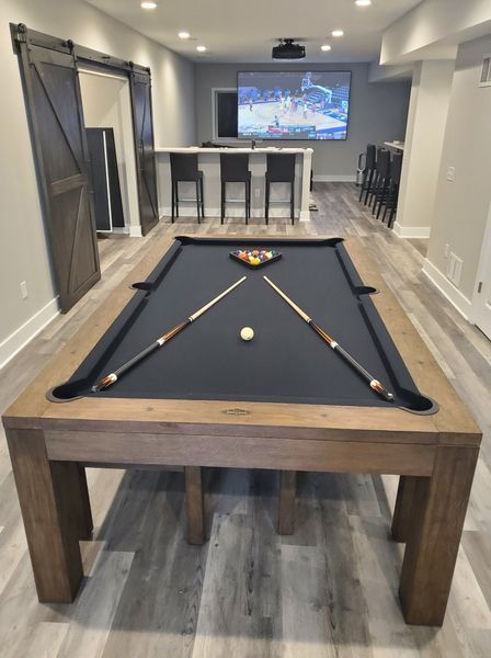 Pool table in a finished basement, with cues and a rack of balls ready to play.