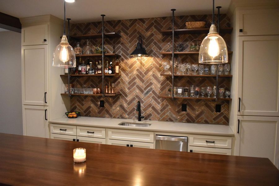 Bar area with a wooden countertop, shelving, and brick backsplash. Clear glass pendant lights illuminate the bar.