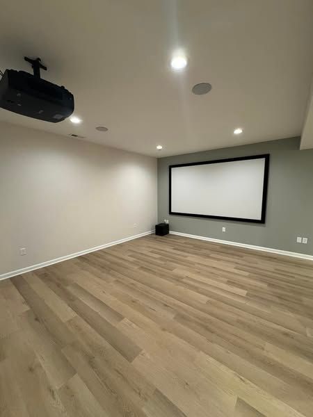 Empty home theater with a projector, screen, speakers, and wood-look flooring.