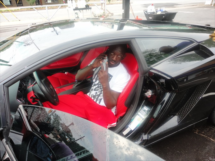 A person sits in the driver’s seat of a black sports car with bright red interior, posing for a photo.