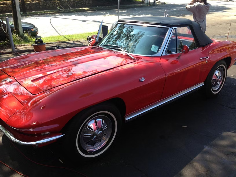 A red vintage Chevrolet Corvette convertible parked on an asphalt surface.