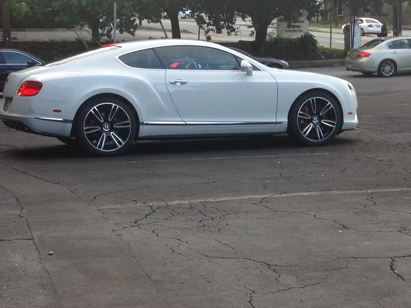 A white Bentley Continental GT coupe parked in an asphalt lot.