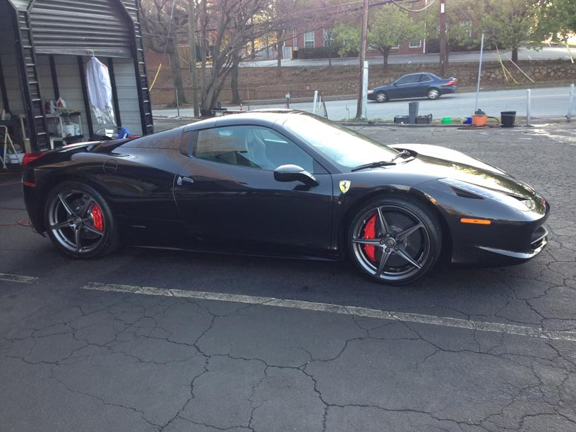 A black Ferrari sports car parked in an outdoor lot on a sunny day.