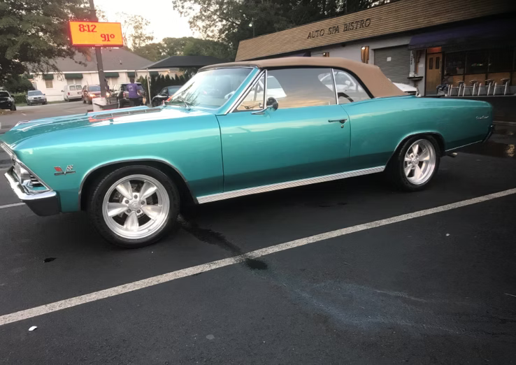 A turquoise convertible classic car parked in an asphalt lot at dusk.