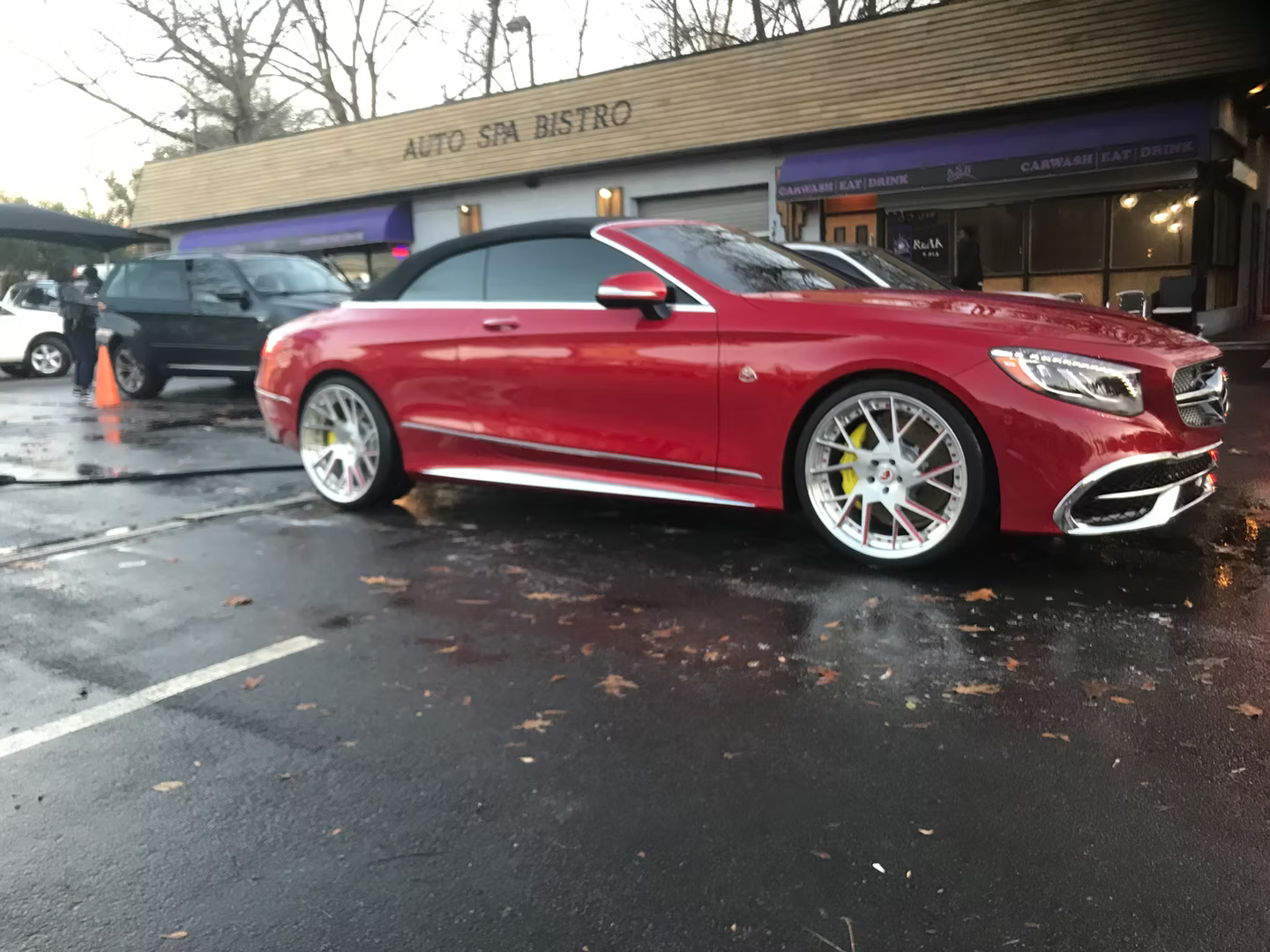 A bright red convertible Mercedes-Benz parked on wet pavement in front of an Auto Spa Bistro building.