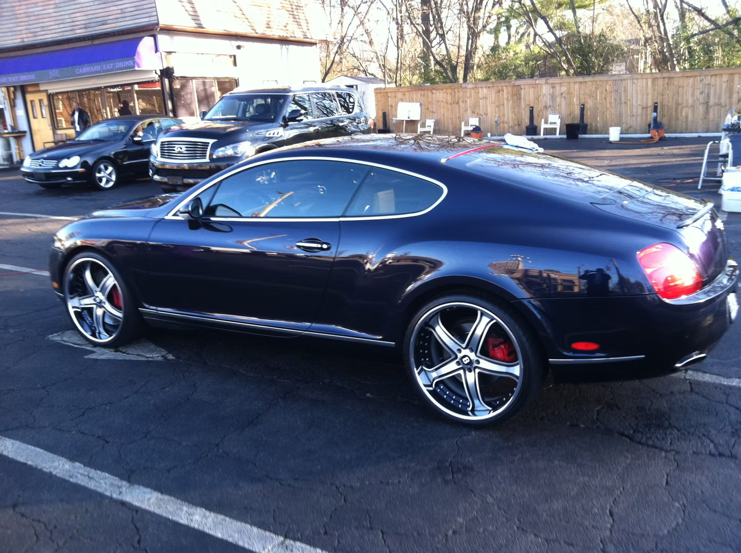 A dark blue Bentley Continental GT coupe parked in an outdoor lot with chrome aftermarket wheels.