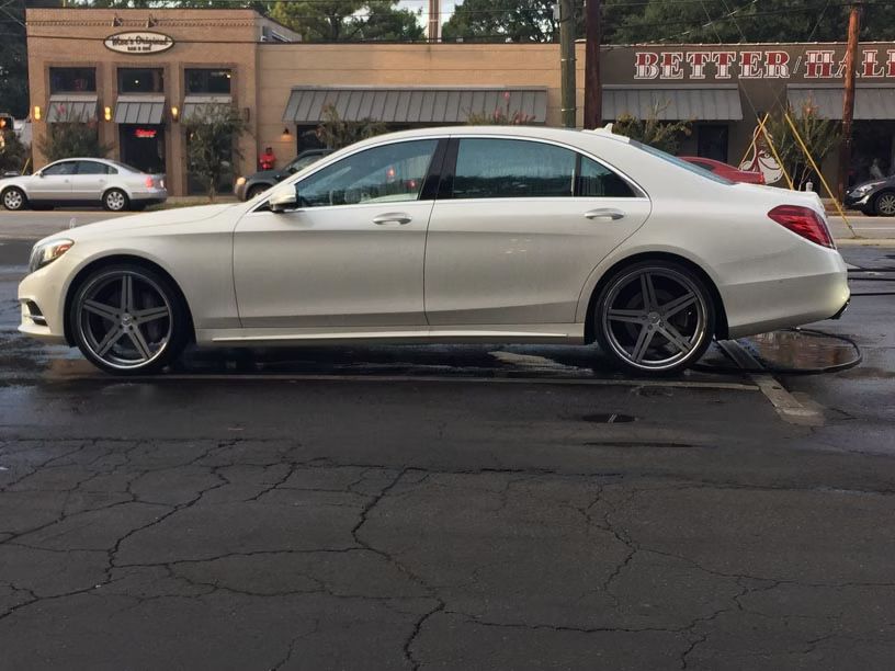 A white luxury sedan parked on a paved lot in front of commercial buildings.