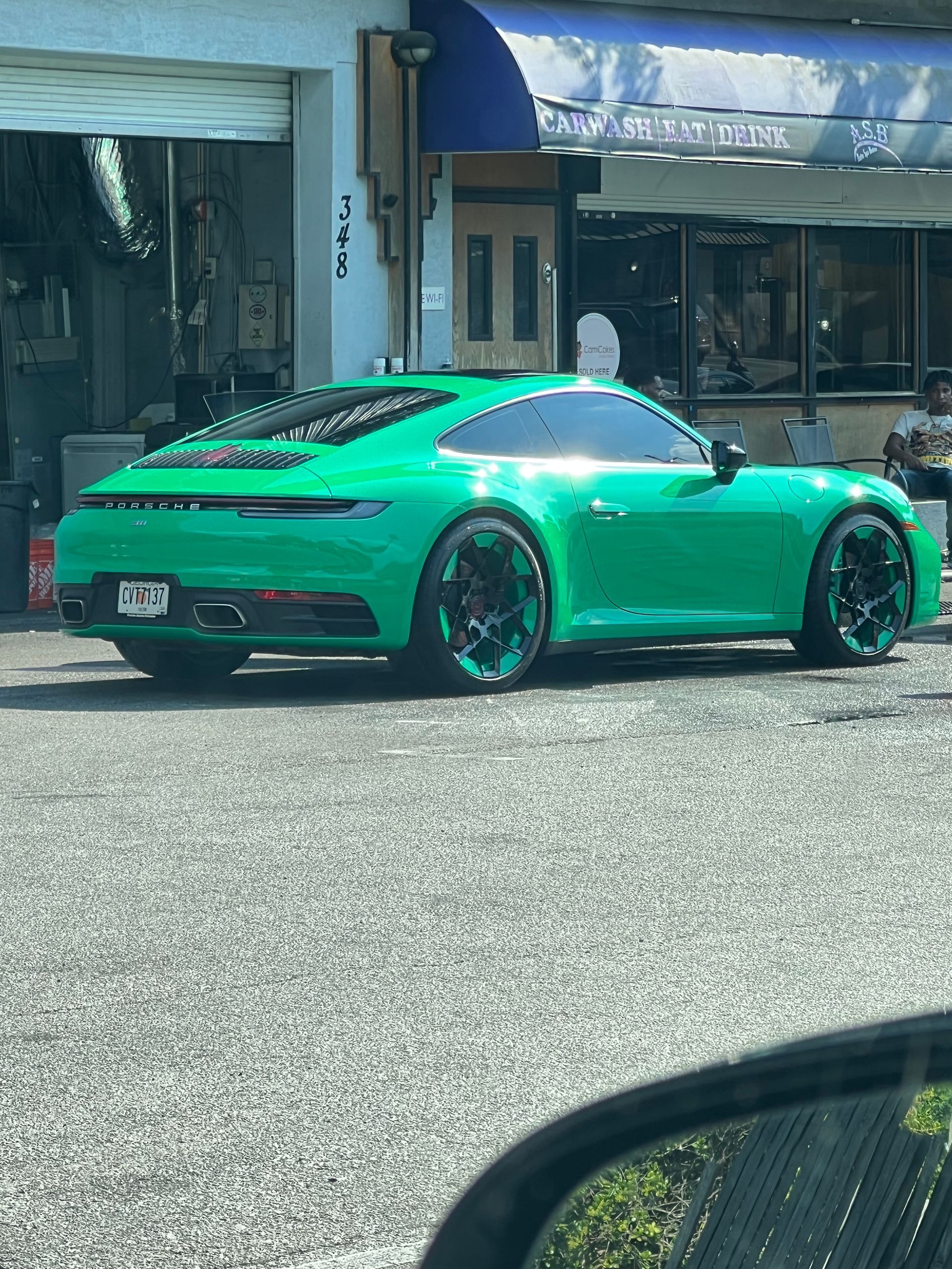 A vibrant green Porsche 911 parked in front of a building with a blue awning on a sunny day.