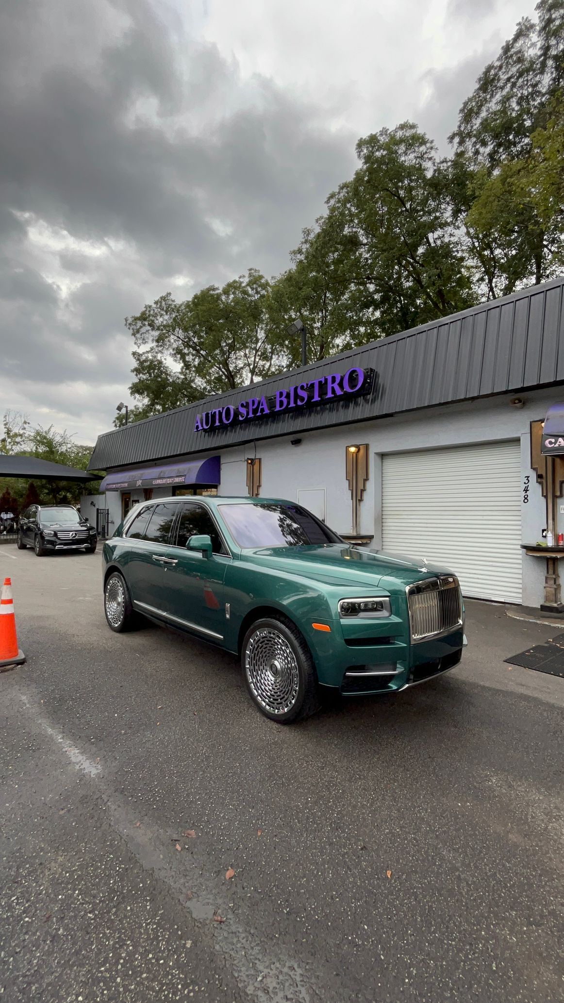 A deep green Rolls-Royce Cullinan parked outside a building.