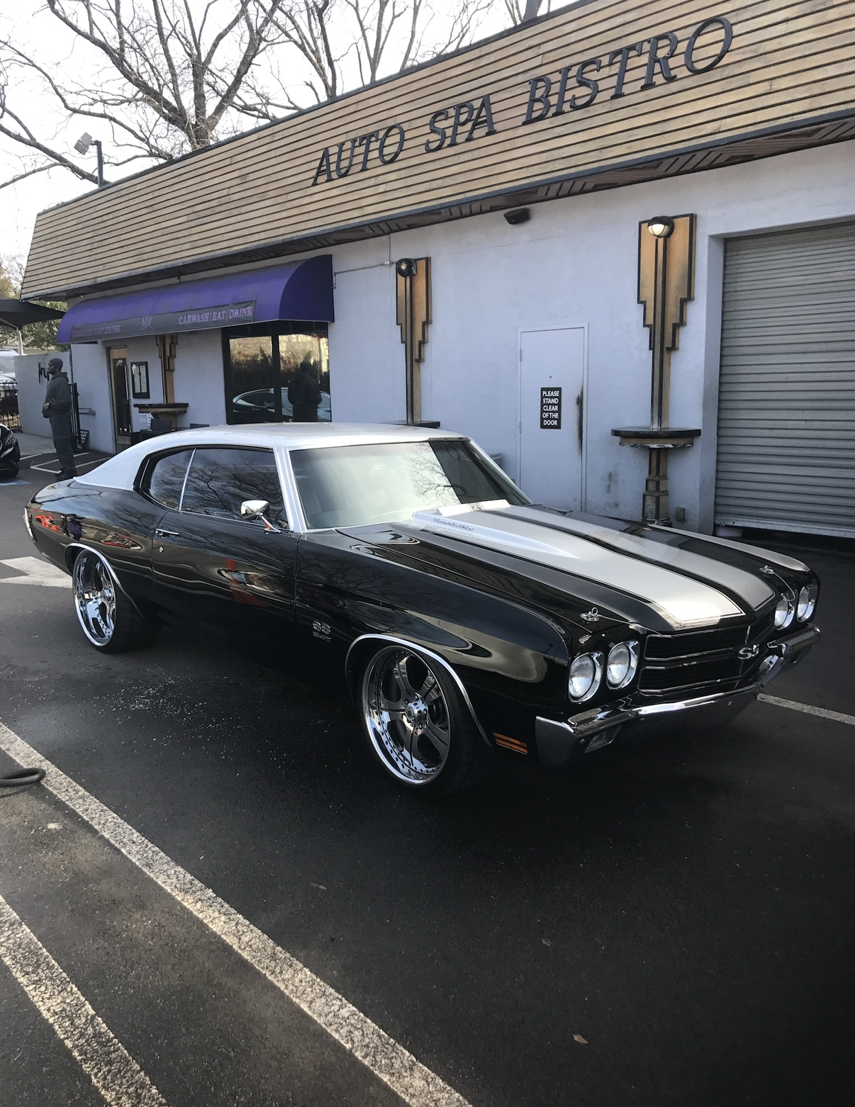 A black and white classic Chevrolet Chevelle SS parked in front of a building named Auto Spa Bistro.