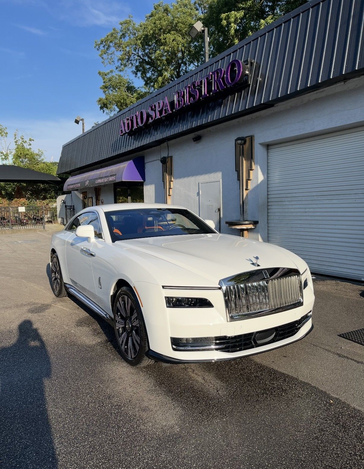 A white Rolls-Royce coupe parked in front of a business building with a purple awning.