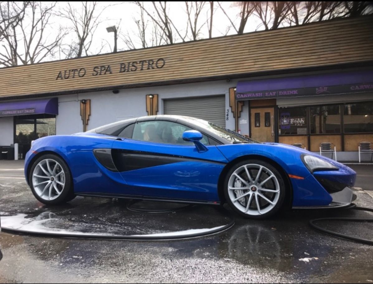 A bright blue McLaren sports car parked in front of the Auto Spa Bistro building during a car wash.