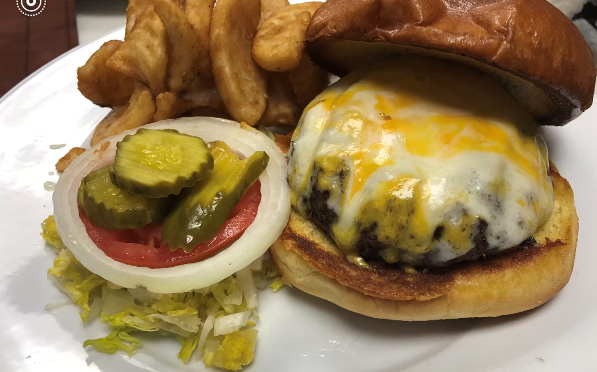 Cheeseburger with melted cheese, tomato, onion, pickles, and lettuce on a bun, served with fries.