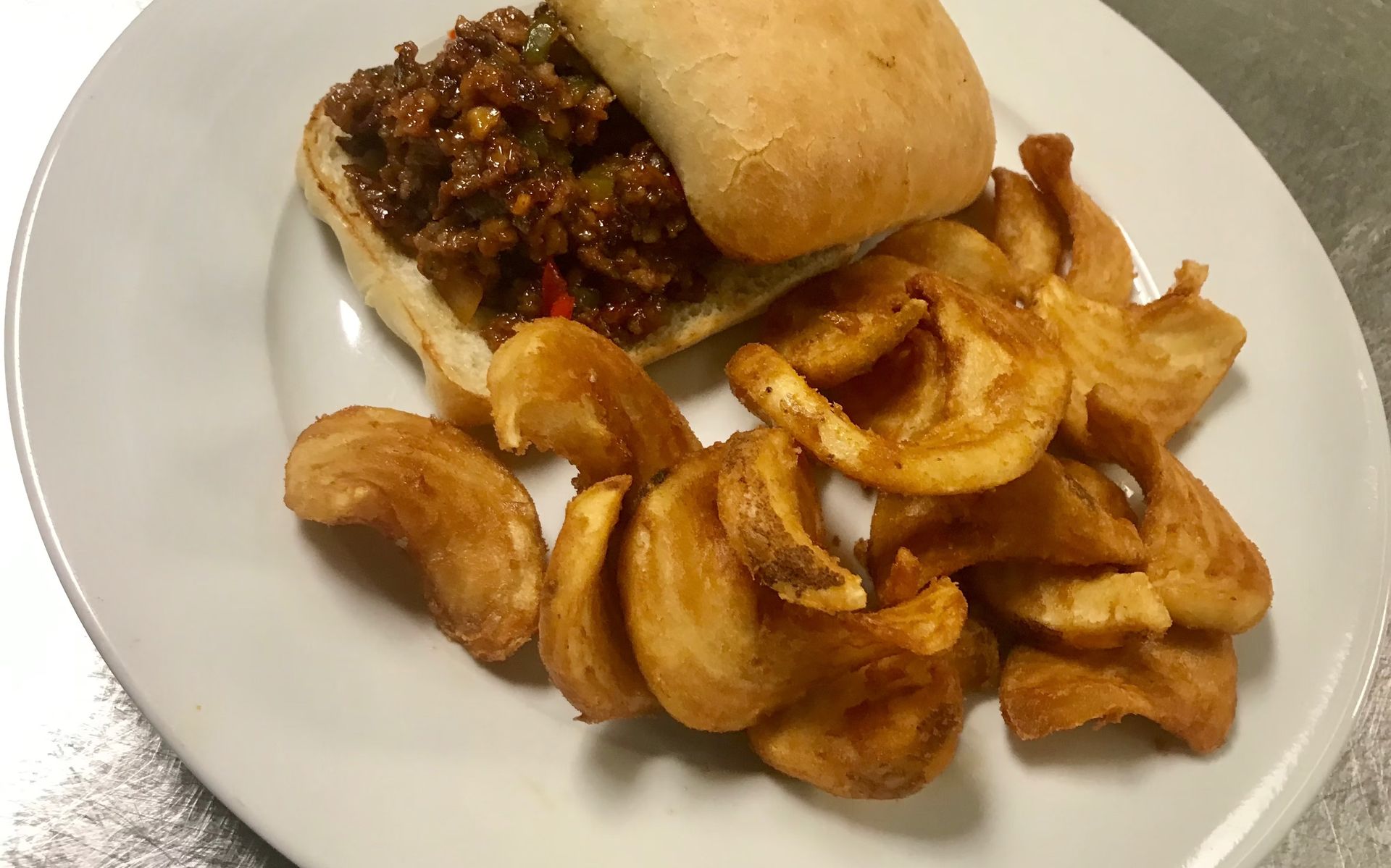 Sloppy Joe sandwich with curly fries on a white plate.