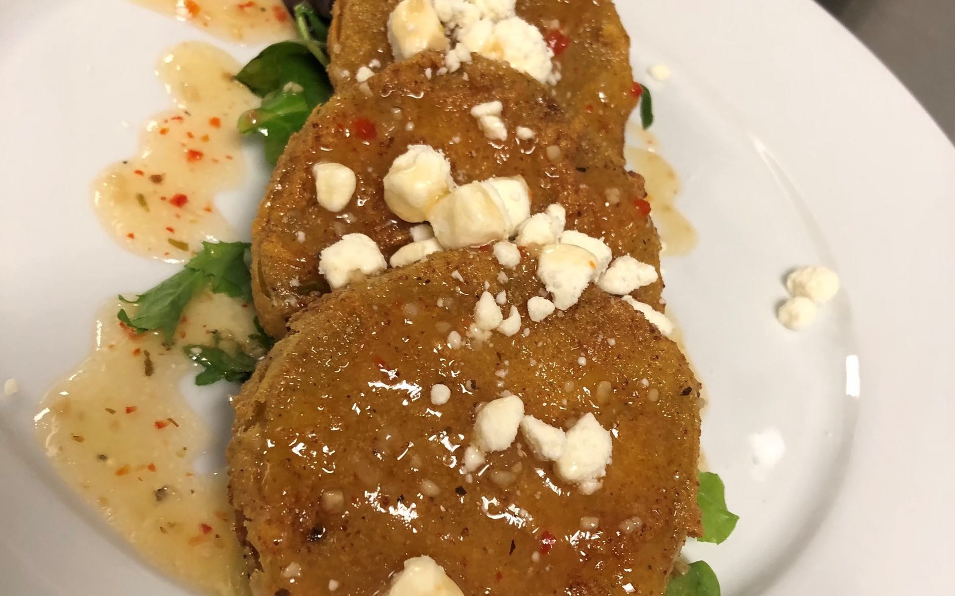 Fried green tomatoes with crumbled cheese and sauce on a white plate.