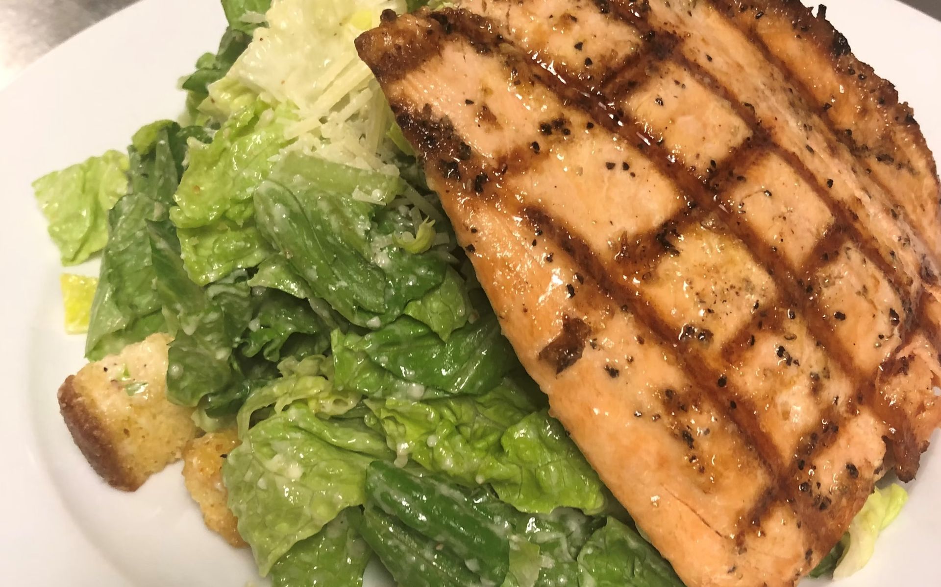 Grilled salmon fillet over Caesar salad, on a white plate.