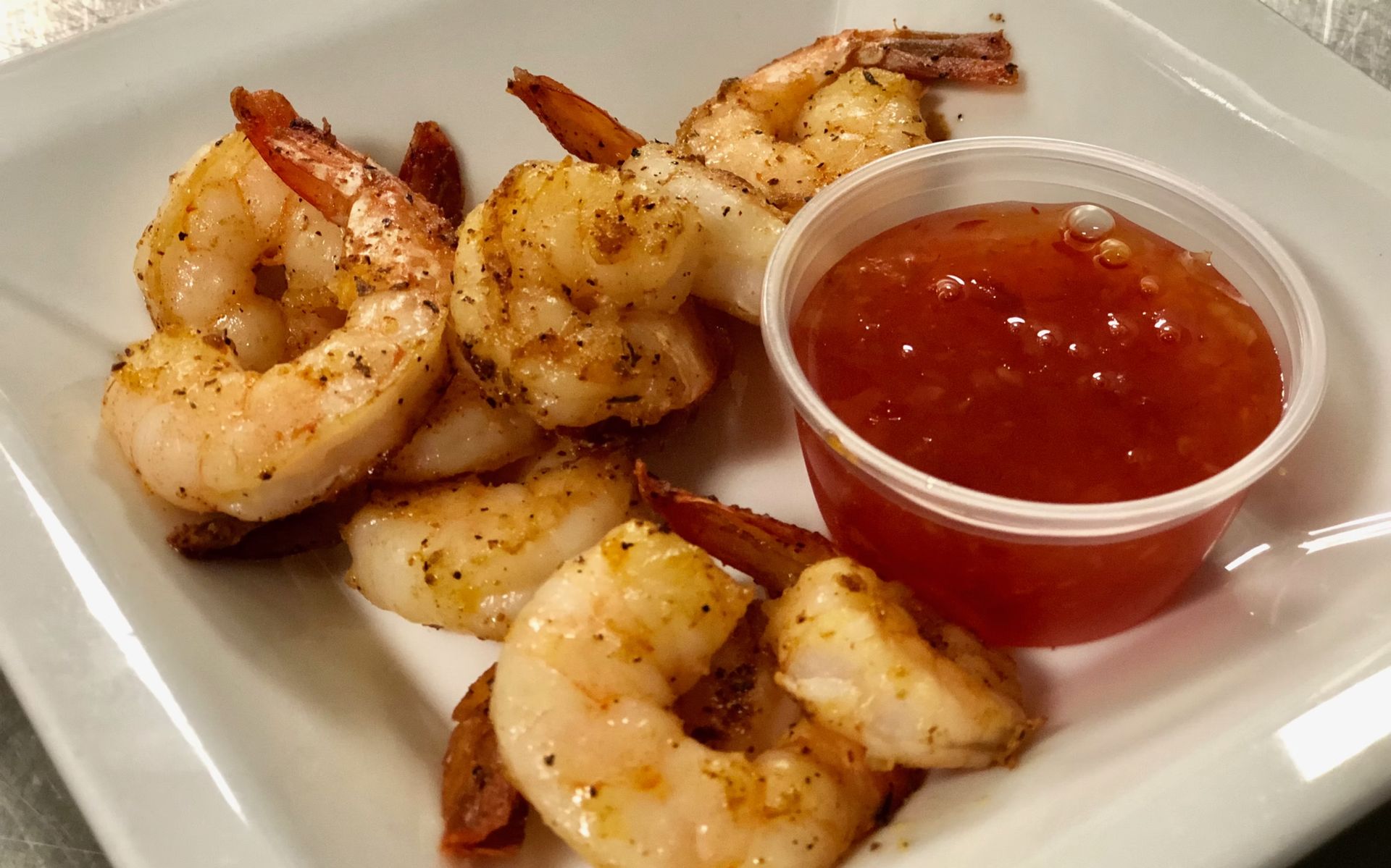 Cooked shrimp with red sauce in a small cup on a white plate.