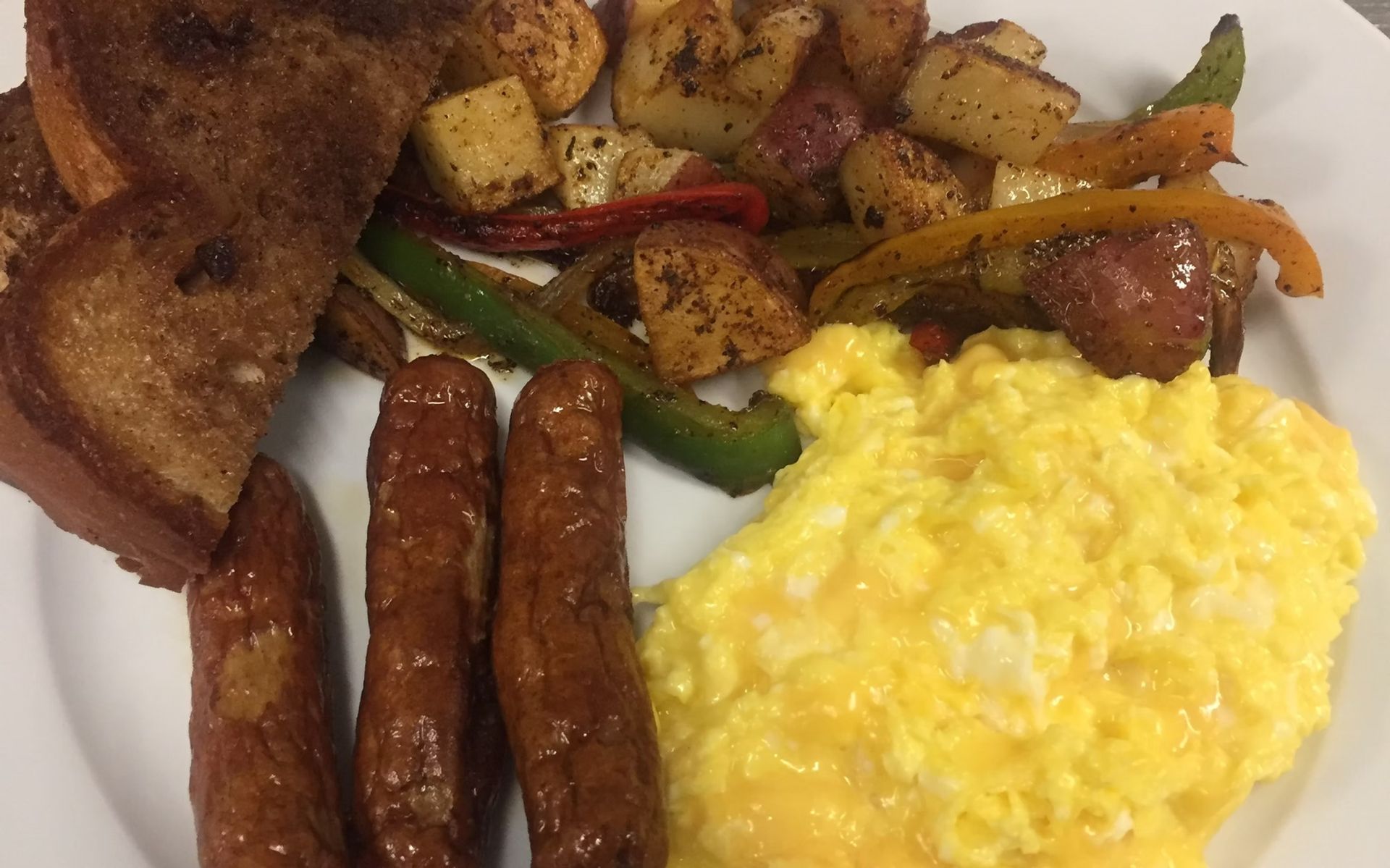 Breakfast plate: scrambled eggs, sausage, toast, and roasted potatoes with peppers.