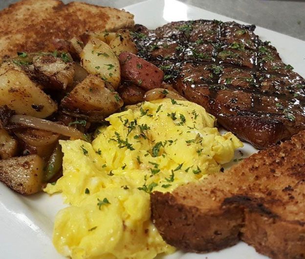 A plate featuring a grilled steak, a pile of scrambled eggs, roasted potatoes, and two slices of toasted bread.