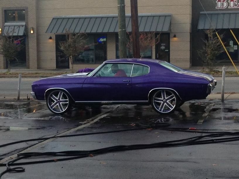 Purple classic car with chrome wheels parked near a building.