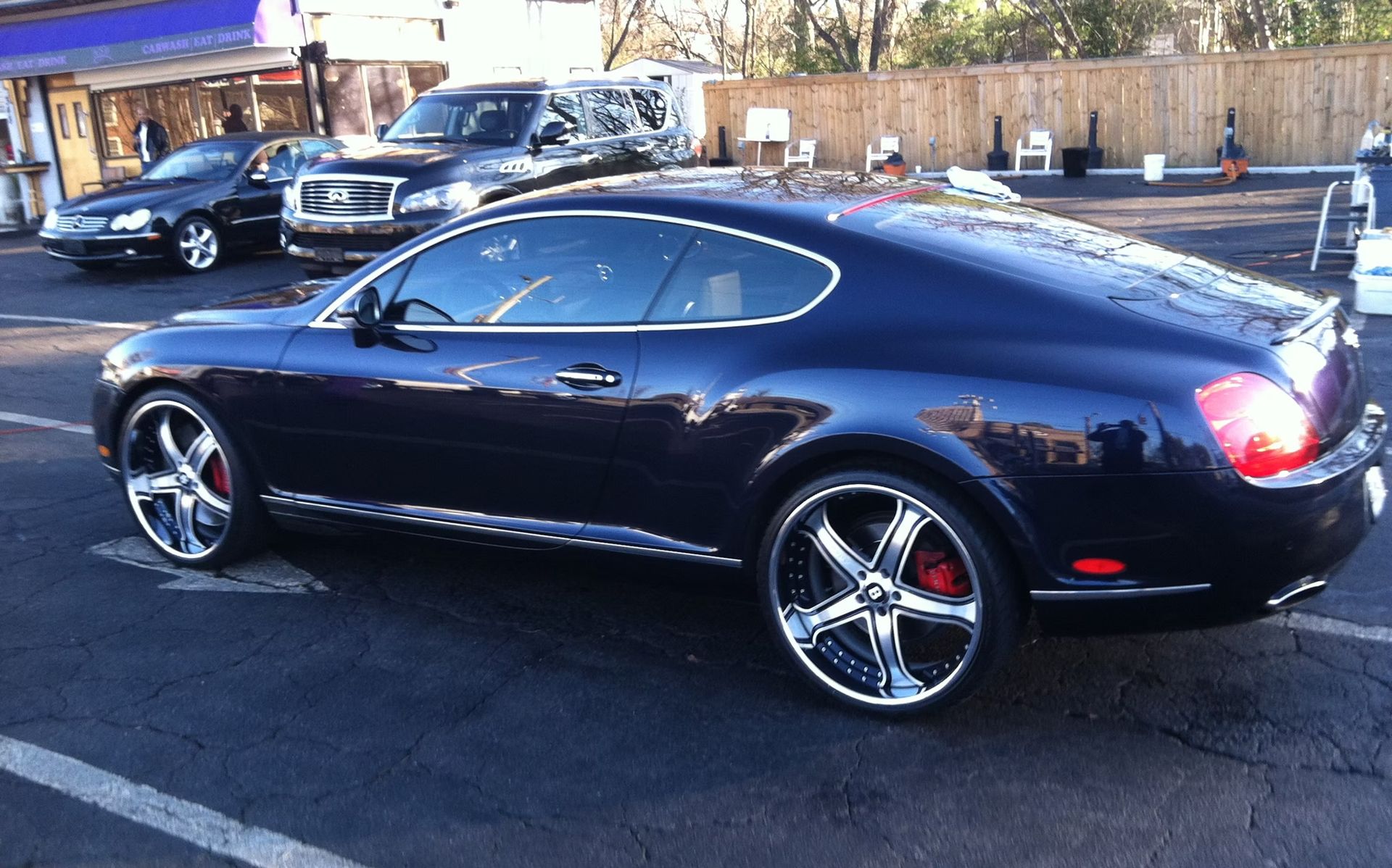 Dark blue Bentley coupe with chrome wheels and red brake calipers in a parking lot.